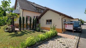 Ein zweistöckiges Haus mit Ziegeldach, einer kleinen angebauten Garage und einem Schild, das es als Ferienwohnung kennzeichnet.