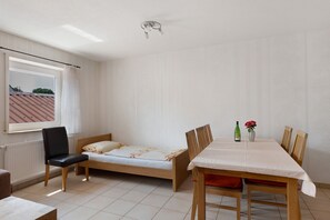 A bedroom with a single bed, a table with chairs, a window with curtains, and a radiator.
