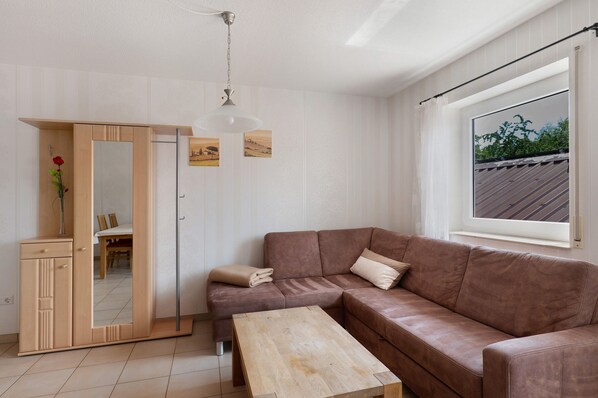 A modern living room with a brown sofa, a wooden coffee table, a mirror cabinet, and a large window with a view.