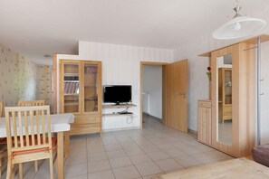 A room with a dining table, chairs, a TV, a wardrobe, and a mirror.