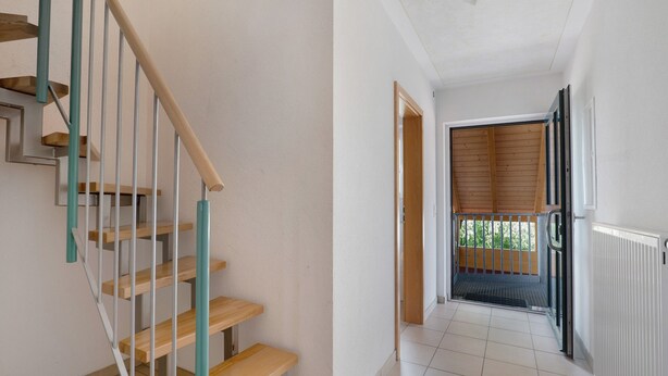 Eine Treppe mit Holzboden und Metallgeländern, eine Tür zu einem Balkon und ein Heizkörper an der Wand.