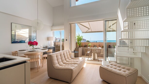 A modern interior with a sofa, dining area, and a view of the sea.