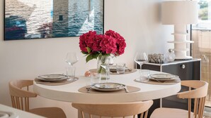 A round dining table with a vase of pink flowers, clear glasses, and plates set for a meal.