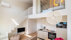 A modern apartment with a staircase, a kitchen, a living area with a sofa, and a dining area.