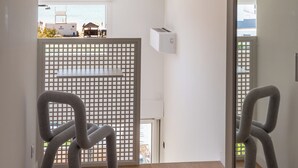 A modern interior with a wooden floor, a white wall, and a view through a window to the outside.