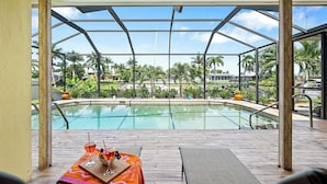 Ein Poolbereich mit Glasveranda, Holzterrasse und Liegestühlen.