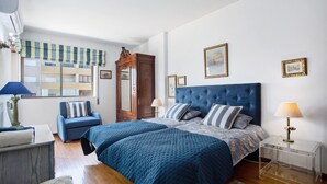 Une chambre avec deux lits, une chaise, une table de chevet, une lampe, une fenêtre donnant sur un beau paysage et un miroir.