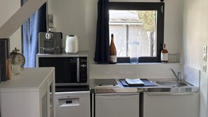 A compact kitchen with a microwave, toaster, and coffee maker on a counter, a sink, and a window with curtains.