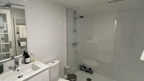 A modern bathroom with a glass shower enclosure, a white sink, and a toilet.