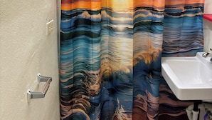 A bathroom with a shower curtain depicting a sunset over the ocean, a sink, and a toilet.