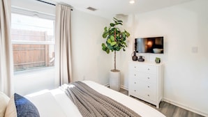 A bedroom with a bed, a dresser, a television, and a potted plant.