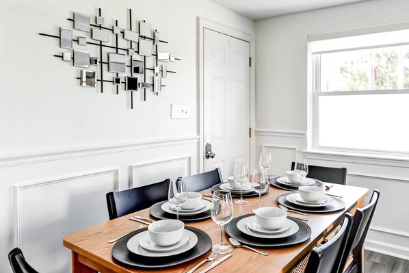 A dining room with a wooden table set for six, black and white plates, and a modern abstract wall art piece.