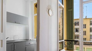 Eine moderne Küche mit grauen Schränken, einer weißen Arbeitsplatte und Blick auf ein gelbes Gebäude durch ein Fenster mit grünen Fensterläden.