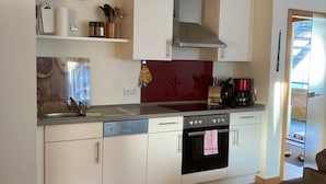 A compact kitchen with a dishwasher, oven, and a clock on the wall. - Apartment 'Erdgeschoss' with Mountain View, Shared Terrace and Wi-Fi (Metzingen)