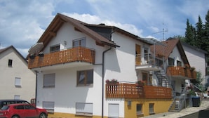 A two-story building with balconies, a staircase, and a red car parked in front. - Apartment 'Erdgeschoss' with Mountain View, Shared Terrace and Wi-Fi (Metzingen)