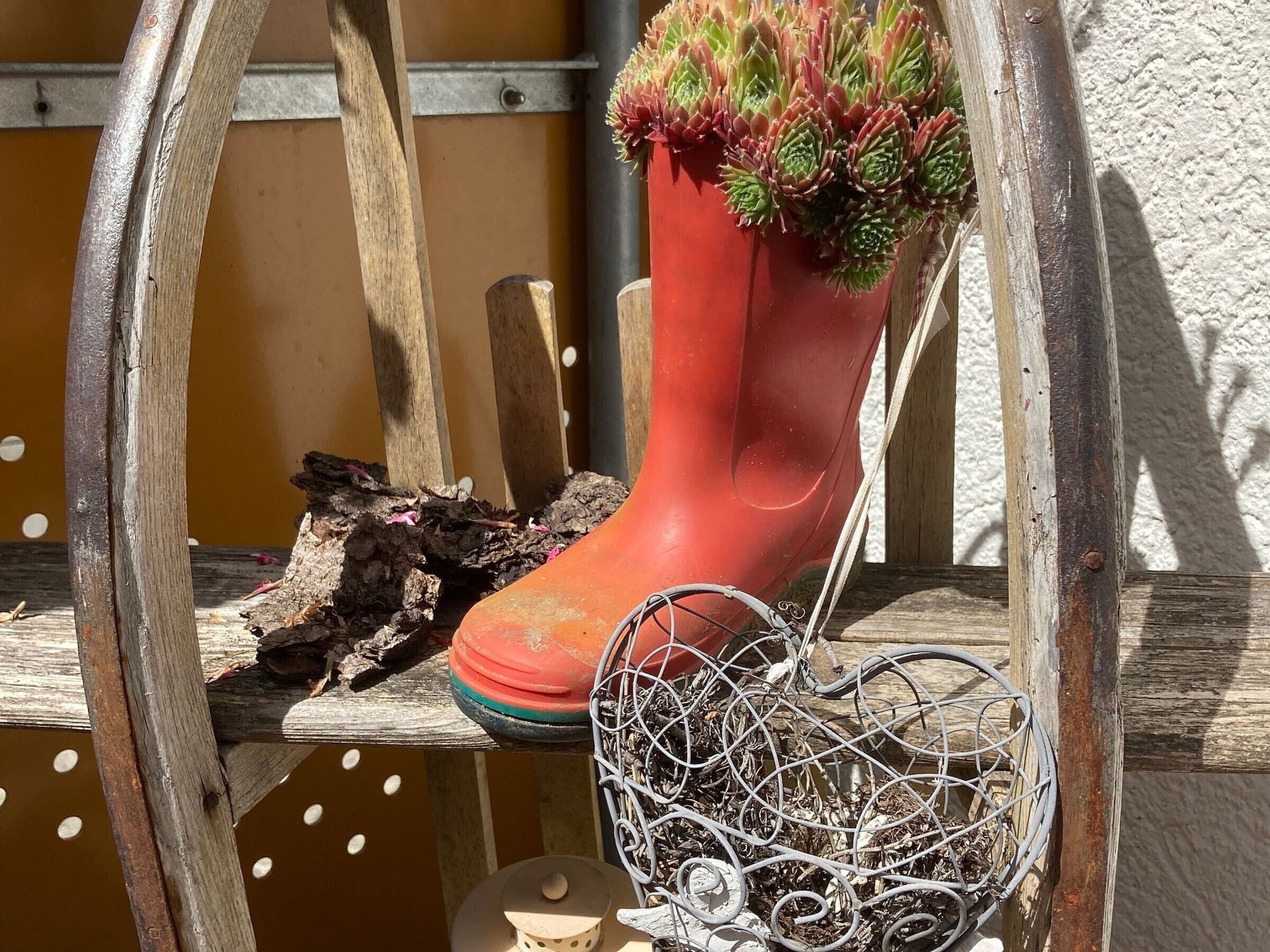 Una jardinera en forma de bota roja con suculentas, una jaula de pájaros metálica y un banco de madera.
