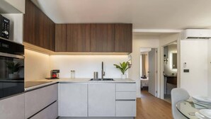 Una cocina moderna con una isla central, armarios empotrados y un comedor con mesa de vidrio.