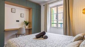 Un dormitorio con una cama, un escritorio, una silla, una planta en maceta y una ventana con cortinas.