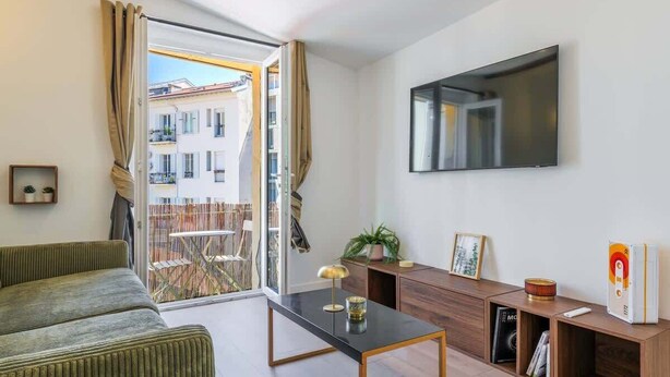 Una sala moderna con un sofá, una mesa de centro, un televisor y un ventanal corredizo que da a un balcón.