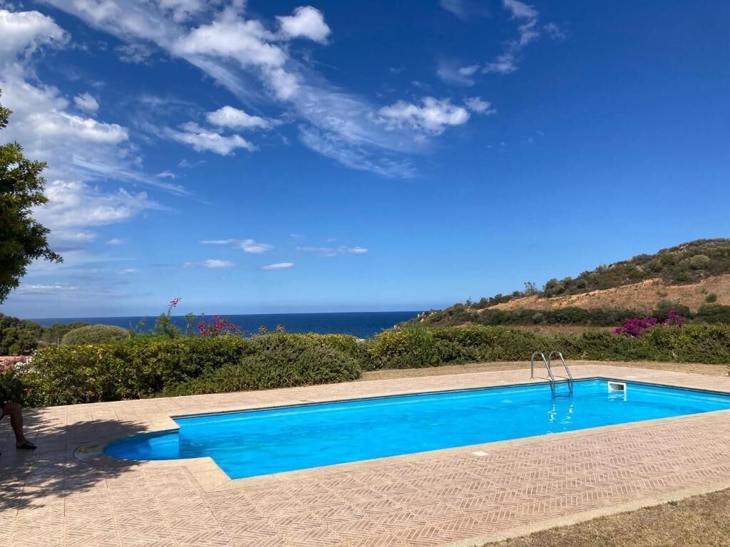 A rectangular swimming pool with a clear blue sky and distant view of the ocean.