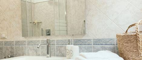 Une salle de bain avec un lavabo, un miroir et une douche. On y trouve des serviettes et un panier sur le comptoir.