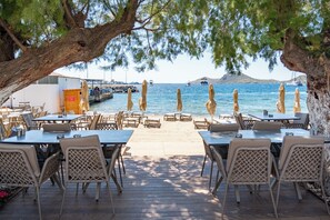 Un restaurant en bord de mer avec une terrasse, une vue sur l’océan et un quai en arrière-plan.