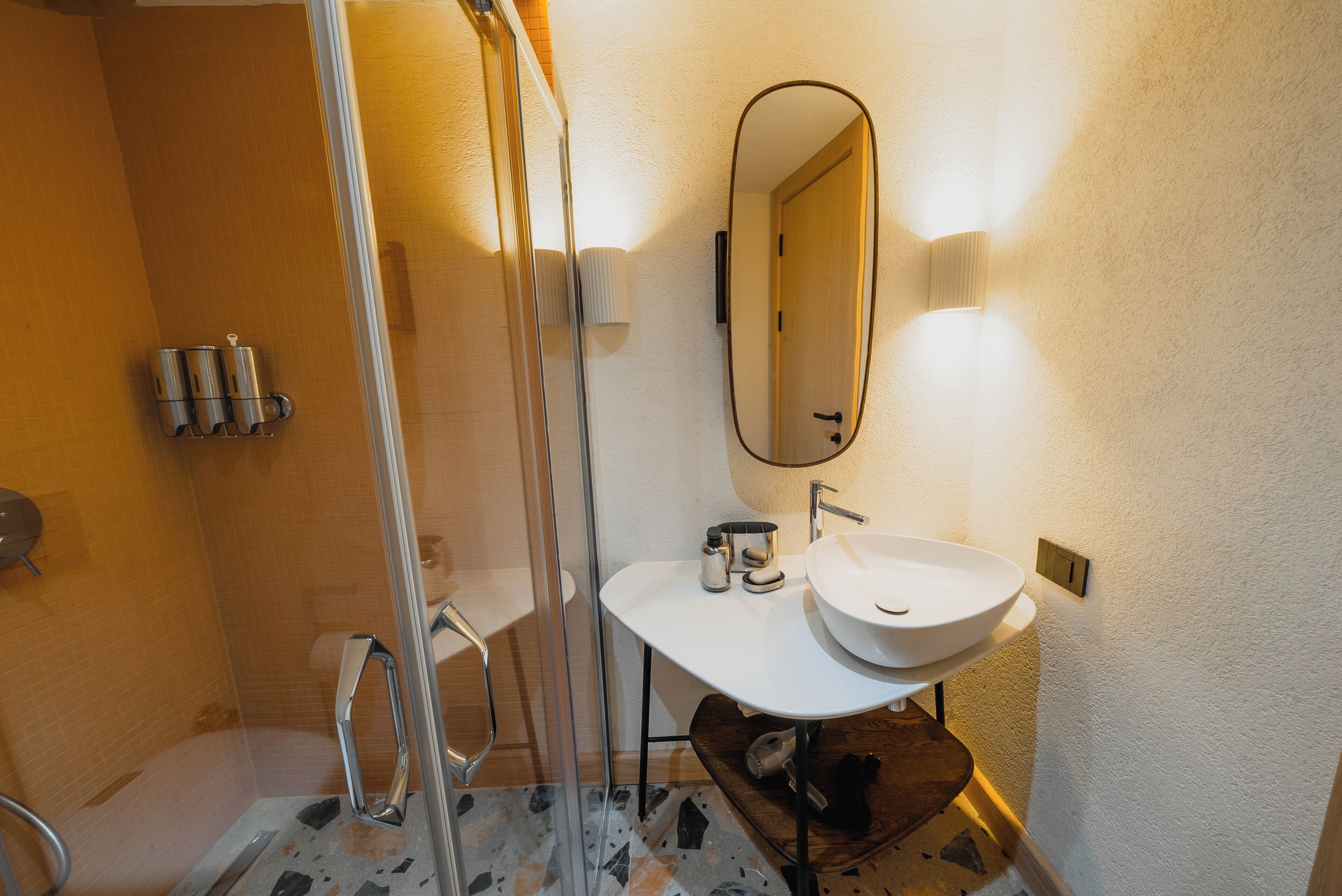 A bathroom with a glass shower enclosure, a white sink, and a mirror.