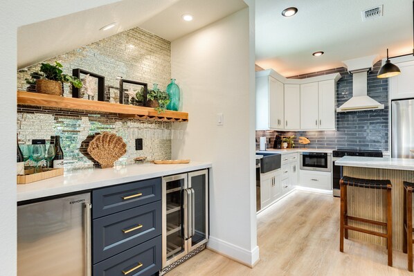 A modern kitchen with a brick backsplash, white cabinets, and a built-in island with bar stools.