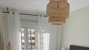 Un dormitorio con una cama grande, una lámpara de pie, un ventanal con cortinas traslúcidas y un radiador.
