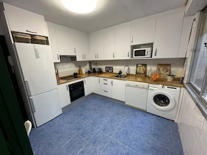 A compact kitchen with white cabinets, a microwave, a sink, a dishwasher, and a washing machine.