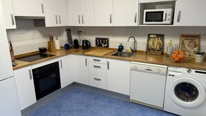 Una cocina moderna con armarios blancos, microondas, fregadero, lavavajillas y lavadora.