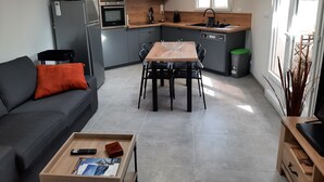 A modern kitchen with grey cabinets, a wooden dining table, and a black sofa with an orange pillow. - T2 house with small adjoining plot, very nice. (Sète)