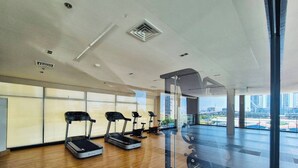 Ett rymligt gym med löpband, en viktbänk och stora fönster med utsikt över staden.