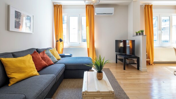 A modern living room with a grey sectional sofa, a white coffee table, and a TV stand. - Spark 2-Bedroom Apartment in Athens (Athens)