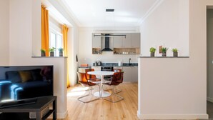 A modern living room with a flat-screen TV, a dining area with a round table and chairs, and a kitchen with wooden cabinets and a built-in stove. - Spark 2-Bedroom Apartment in Athens (Athens)