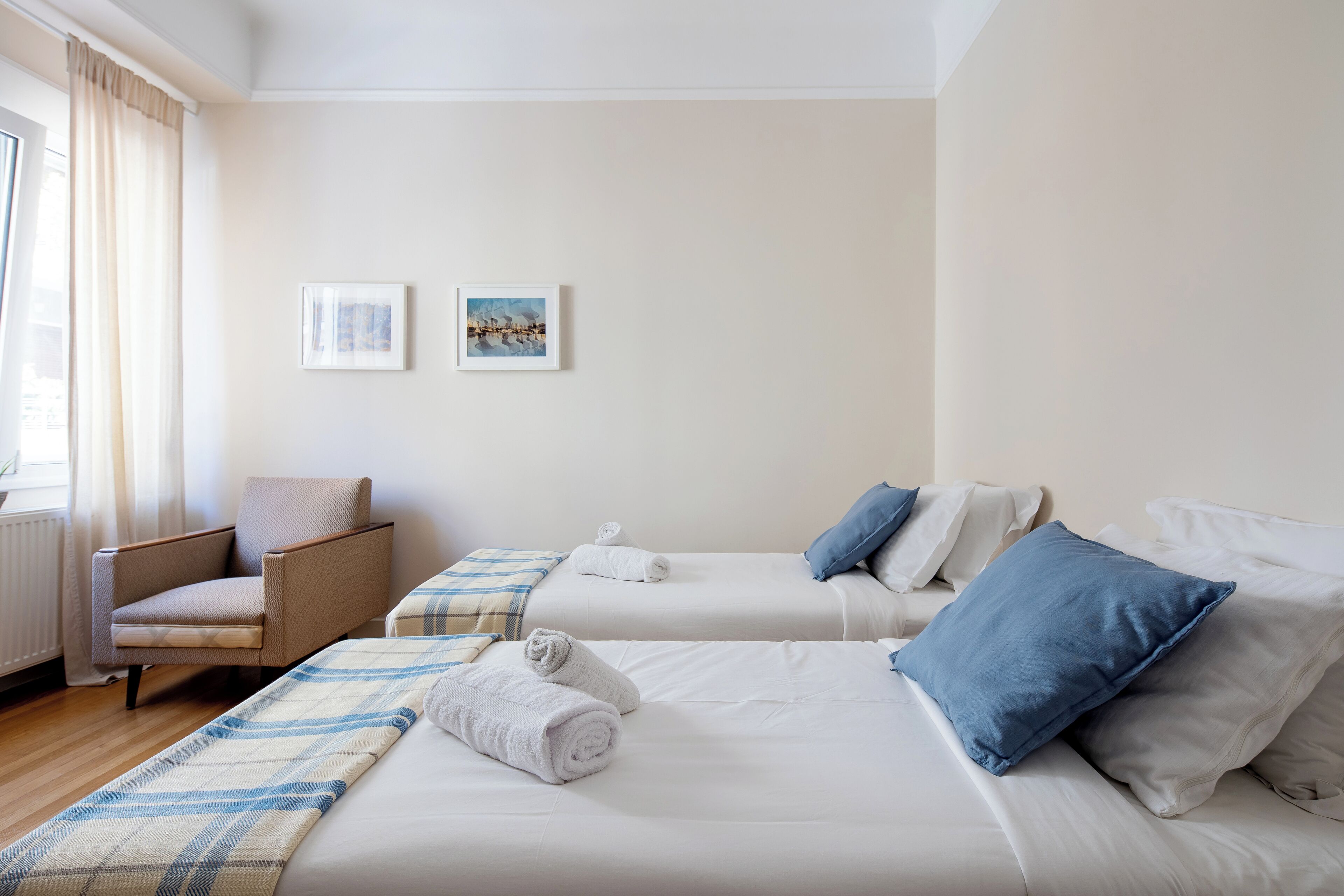 Een hotelkamer met twee bedden, een stoel en twee ingelijste foto's aan de muur.