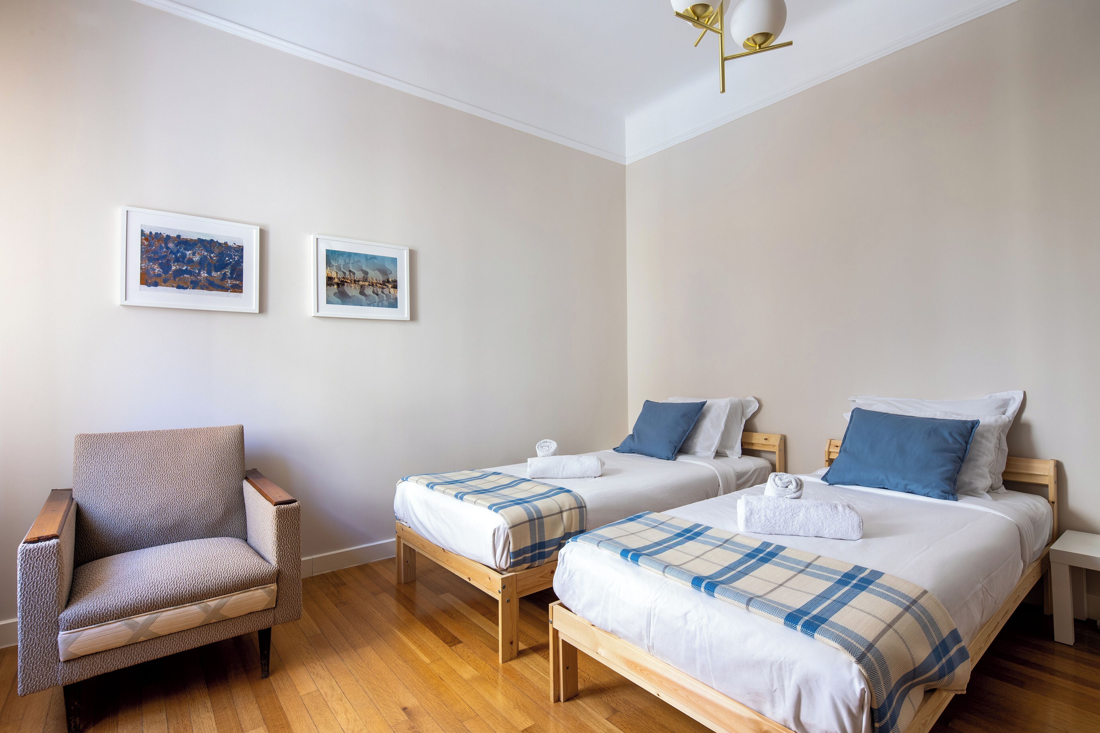 Een hotelkamer met twee eenpersoonsbedden, een houten stoel en twee ingelijste foto's aan de muur.