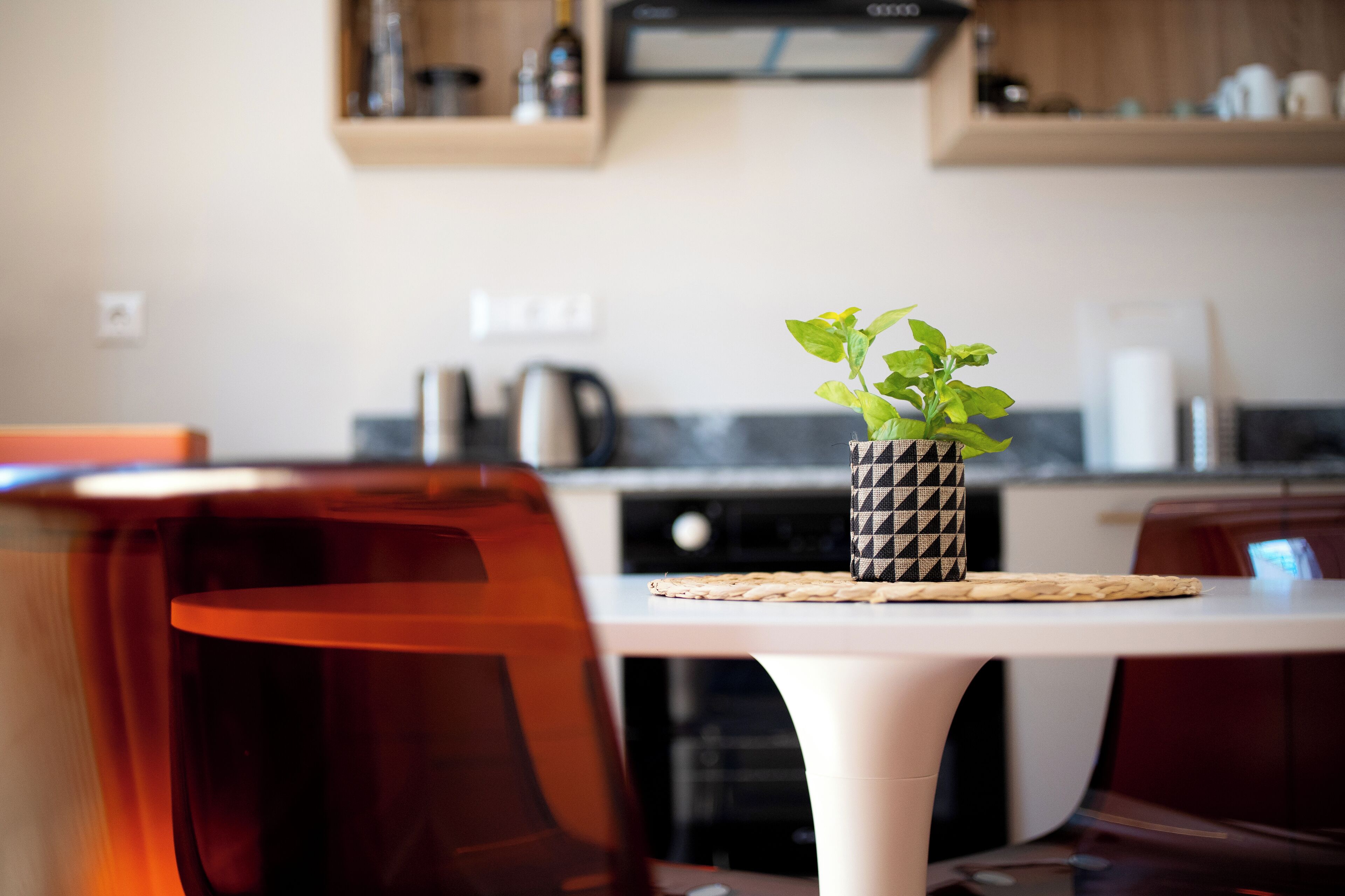 Eine moderne Küche mit einem weißen Tisch, einer Pflanze in einer gemusterten Vase und einer Kaffeemaschine.