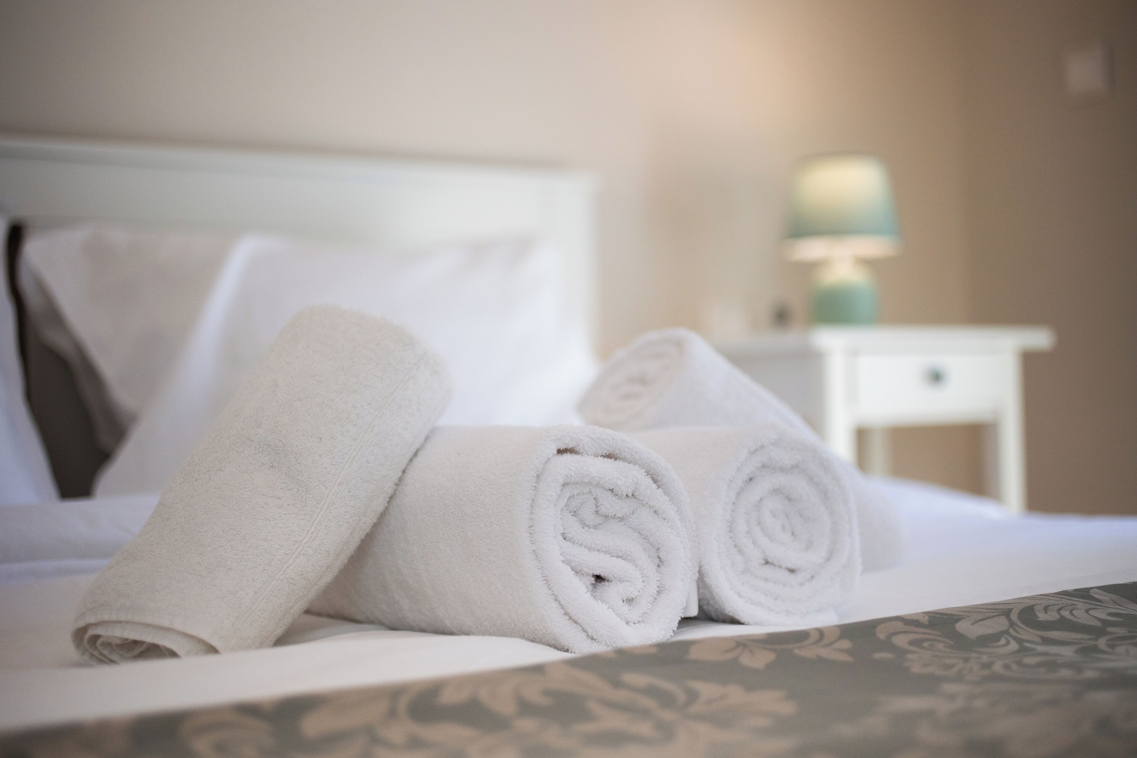 A neatly made bed with rolled white towels and a bedside table with a lamp.