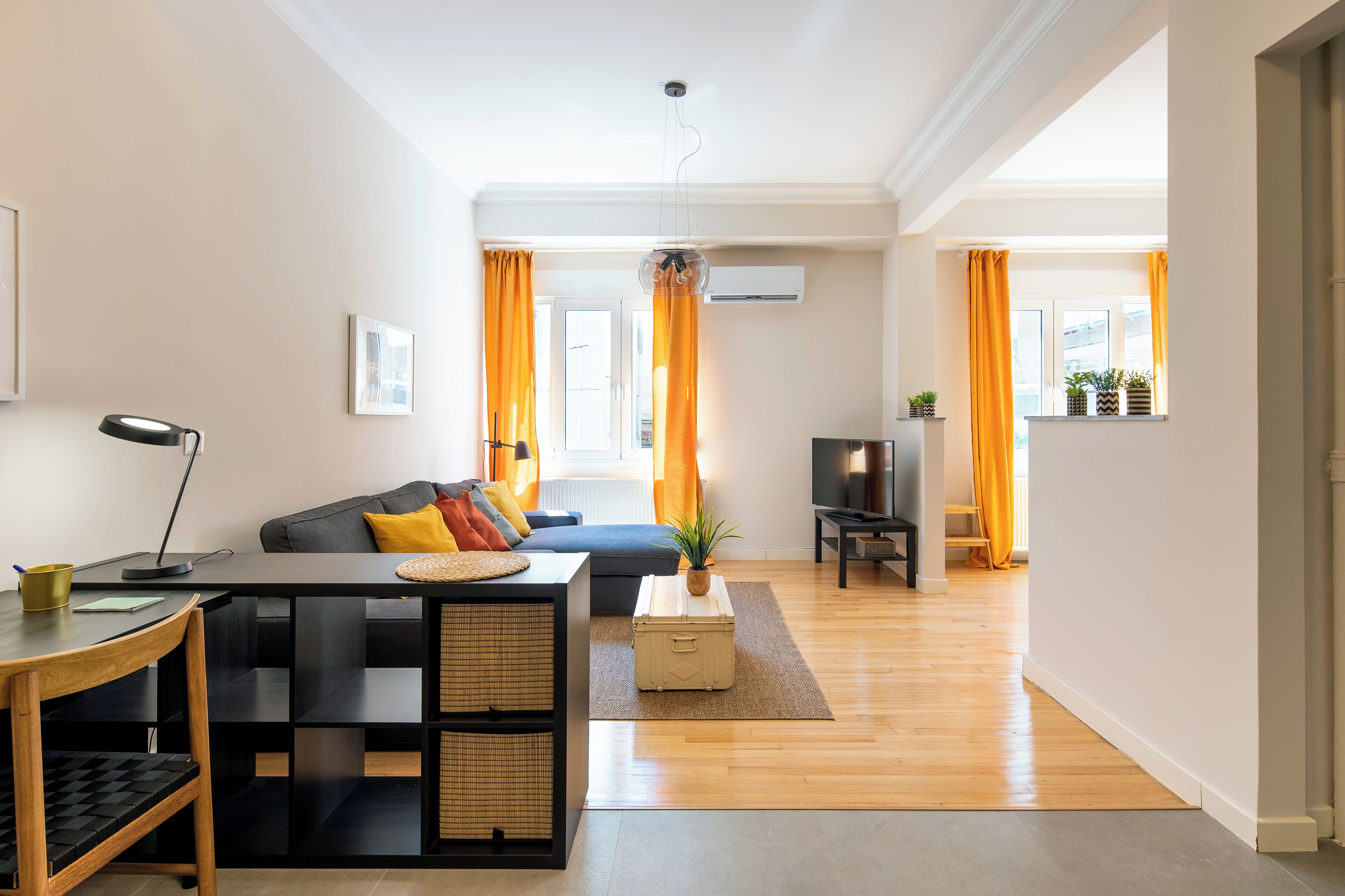 A modern living room with a sofa, a coffee table, a TV, and a desk with a lamp.