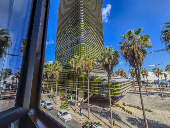 Un edificio moderno con facciata in vetro curvo, circondato da palme e un cielo azzurro limpido.