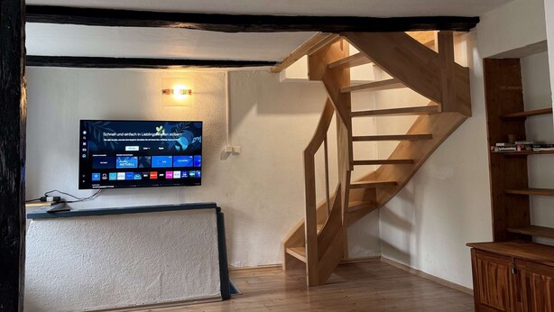 Una habitación con una escalera de madera, un televisor de pantalla plana en la pared y un armario de madera.