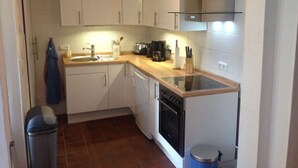 Una cocina compacta con armarios blancos, encimera de madera, estufa y un cubo de basura.