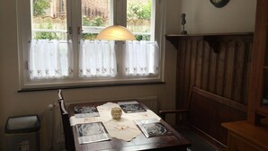 Un rincón comedor con una mesa dispuesta para dos, una ventana con cortinas, un radiador y un reloj en la pared.