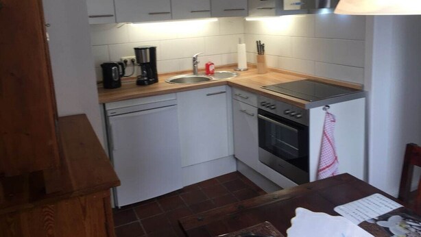 Una cocina compacta con armarios blancos, lavavajillas, horno y cafetera.