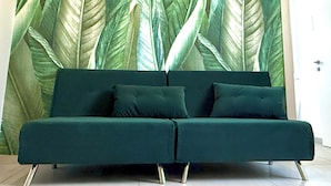 Un canapé vert aux pieds métalliques, placé devant un mur orné d’un grand motif de feuilles.