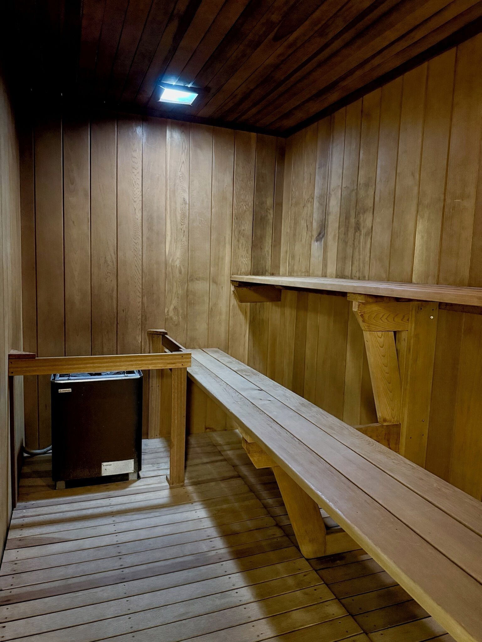 A sauna room with wooden benches, a bench with a heater, and a heater on the floor.
