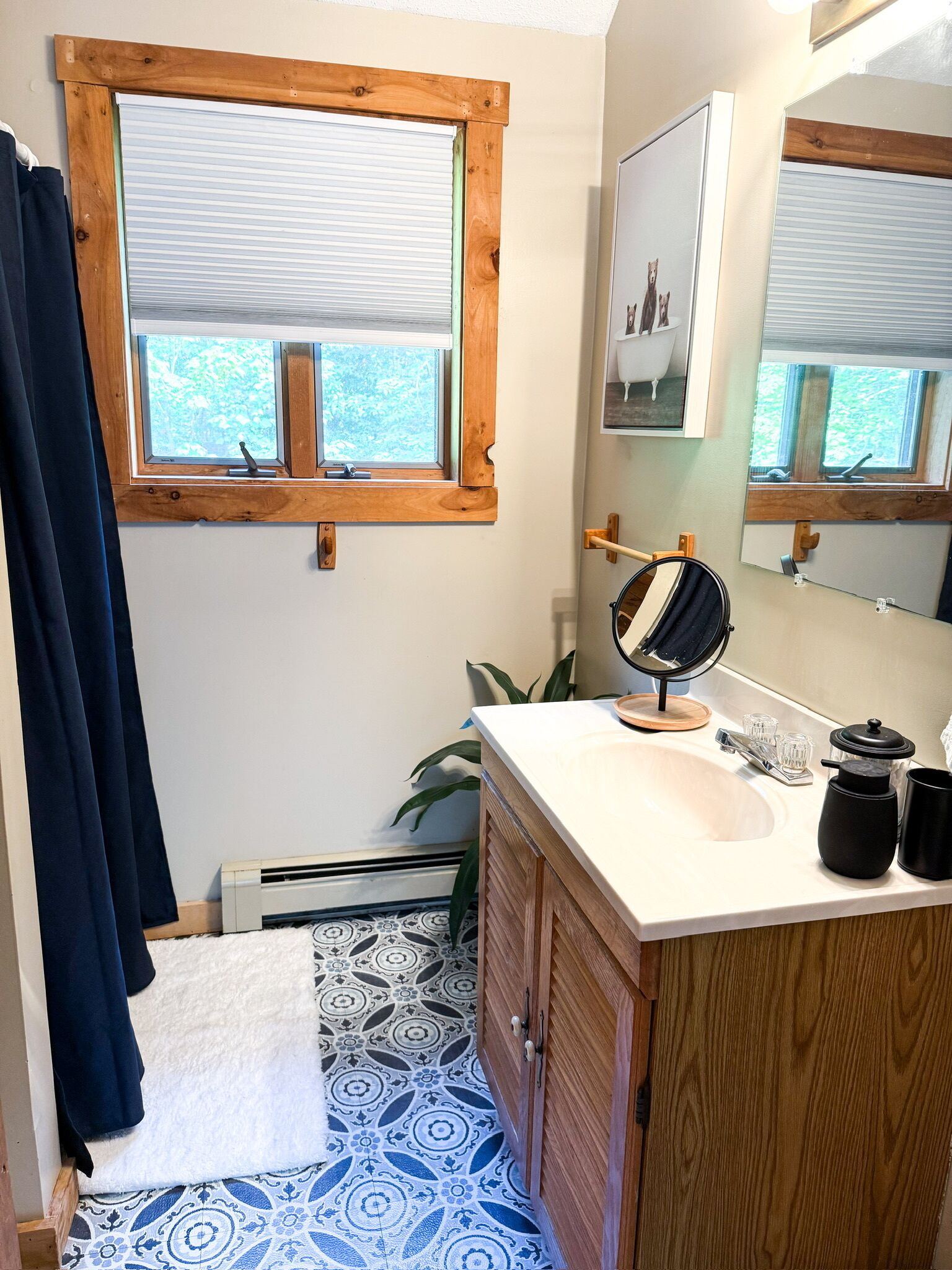 A bathroom with a wooden vanity, a mirror, a sink, and a window with a view of trees.