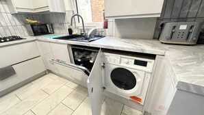 A compact kitchen with white cabinetry, a built-in oven, a dishwasher, and a microwave. - Southsea 5-bed Seaside Retreat- Sleeps 11 & Garden (Portsmouth)