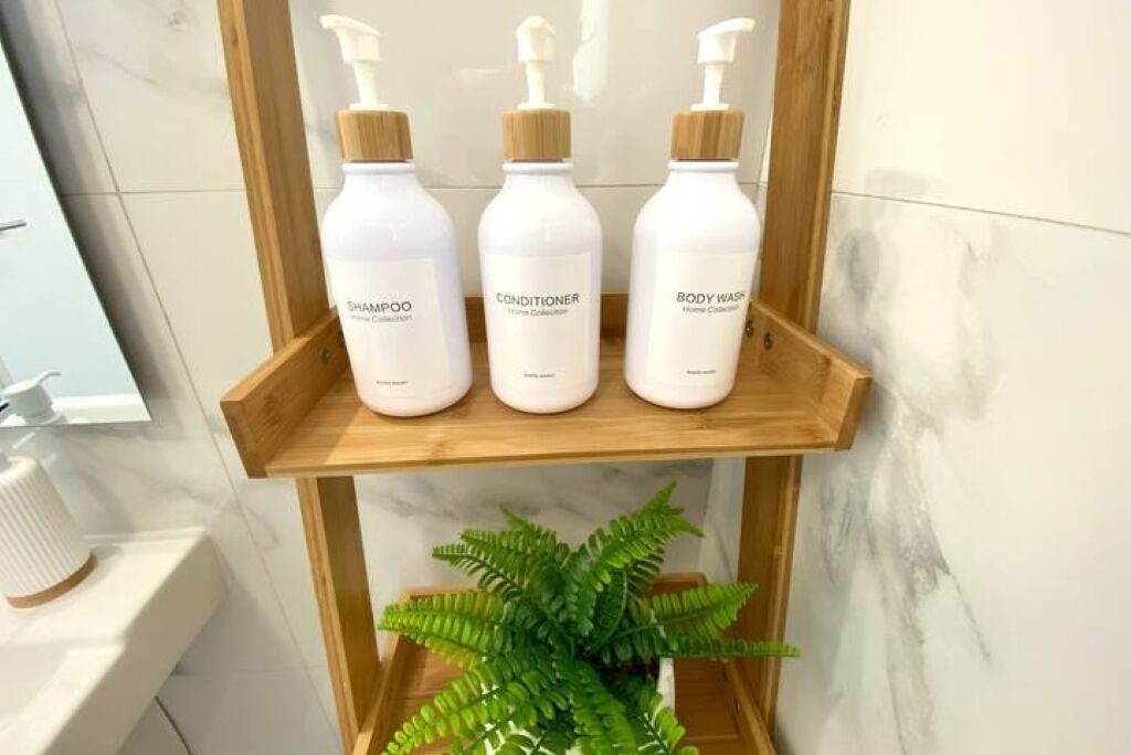 A wooden shelf with three white bottles labeled 'SHAMPOO,' 'CONDITIONER,' and 'BODY WASH.'